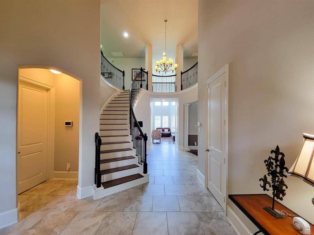 This inviting entryway features a grand curved staircase, high ceilings, and elegant lighting. The open layout leads to a spacious living area with ample natural light. Perfect for a welcoming and stylish home.