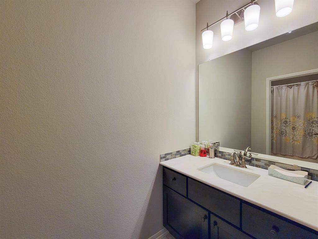 This bathroom features a modern vanity with ample storage, a sleek countertop, and a large mirror. It is well-lit with stylish overhead lighting, and the shower area has a decorative curtain.