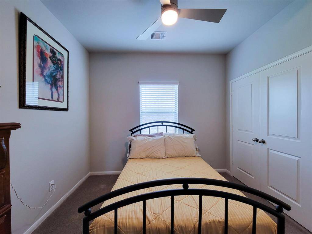 Cozy bedroom with neutral walls, featuring a window for natural light. It includes a double bed, modern ceiling fan, and ample closet space. A colorful framed artwork adds character.