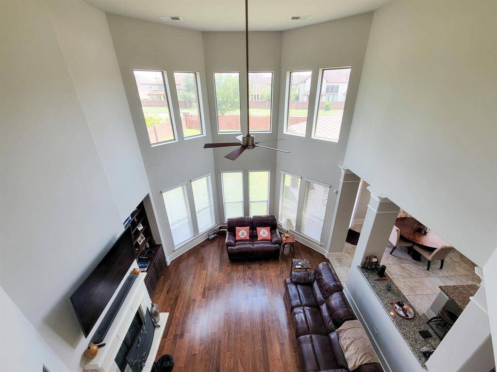 Spacious, open-concept living room with high ceilings and abundant natural light from large windows. It features hardwood floors, a fireplace, and a view into the kitchen area, creating an inviting and airy atmosphere.