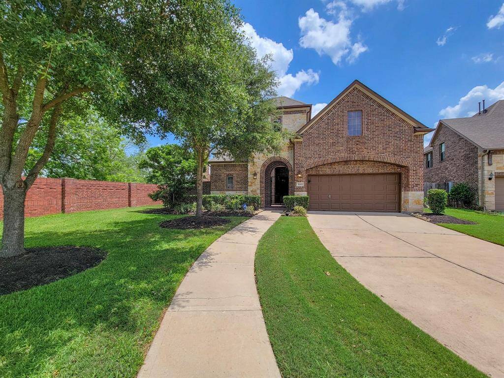 This charming brick home has a two-car garage, a curved driveway, and a well-maintained front yard. Mature trees provide shade, and the house features an inviting front entrance.