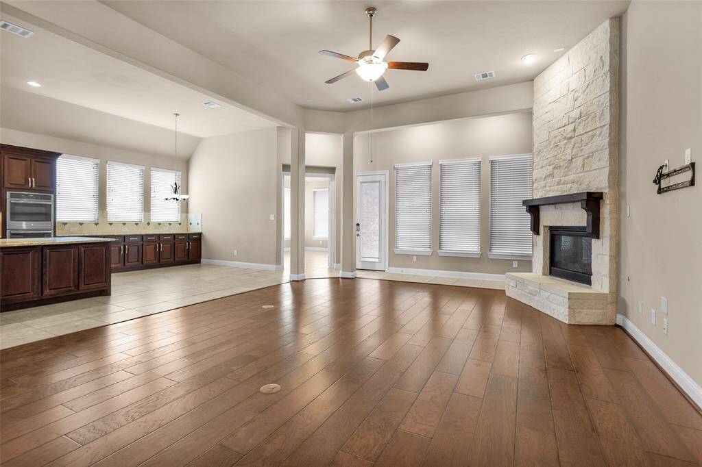 This spacious living area features beautiful hardwood floors, a stone fireplace, and an open layout connecting to a modern kitchen with dark wood cabinets and ample natural light.