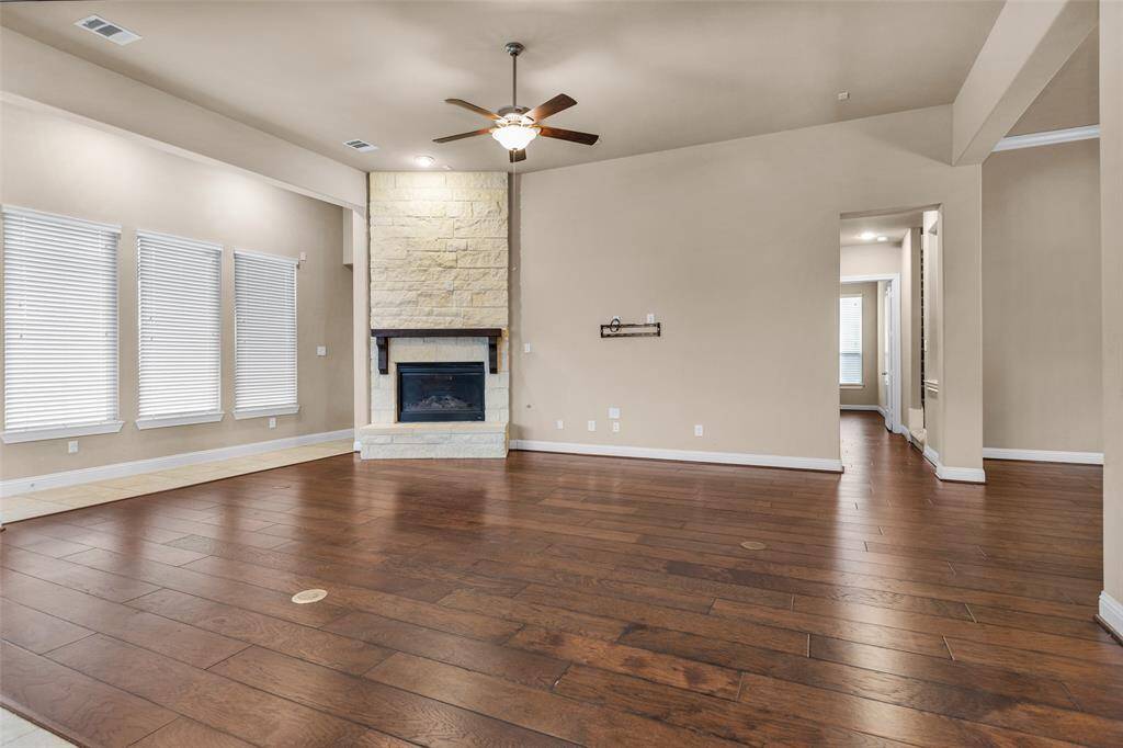 Spacious living room with warm wood flooring, high ceilings, and a beautiful stone fireplace.