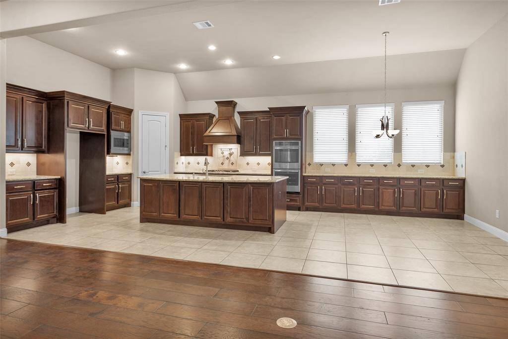 Spacious kitchen with elegant dark wood cabinetry, a huge, eat in island, convenient pot filler, stainless steel appliances with double ovens.
