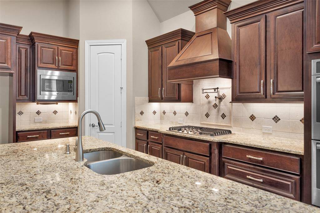 This chef inspired kitchen features elegant wooden cabinetry, granite countertops, and a built-in microwave. It includes a gas cooktop with a stylish range hood, convenient pot filler and a double sink, providing both functionality and modern design.