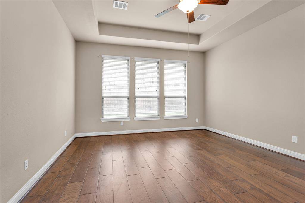 The primary bedroom features hardwood floors, tray ceiling, neutral walls, and has large windows allowing natural light to brighten the space.