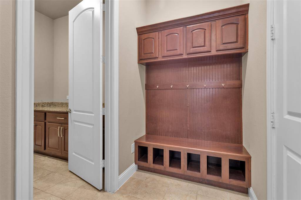 Functional mudroom with built-in wooden storage, including upper cabinets, hooks for hanging, and cubbies below. Adjacent is the laundry. The space is practical for organizing coats, shoes, and accessories.