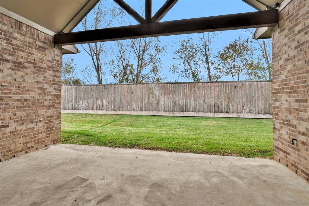 Outdoor living space showcases a covered patio with a brick exterior, opening to a fenced backyard with no neighbors behind.