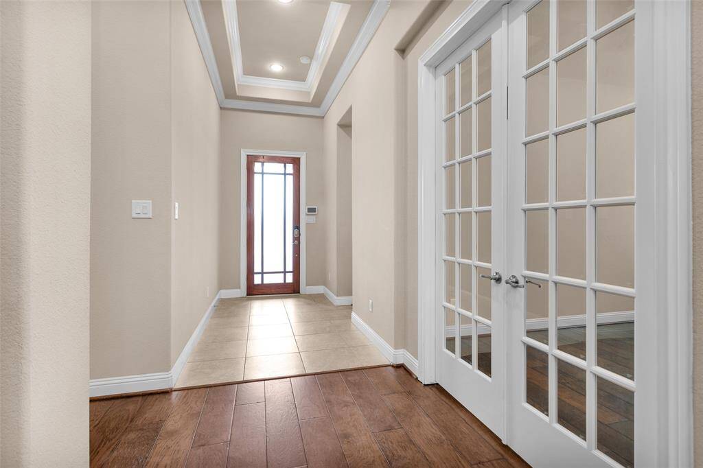 Bright entryway with a mix of tile and wood flooring. Features a glass-paned front door and elegant French doors leading to the study, complemented by recessed lighting and crown molding.