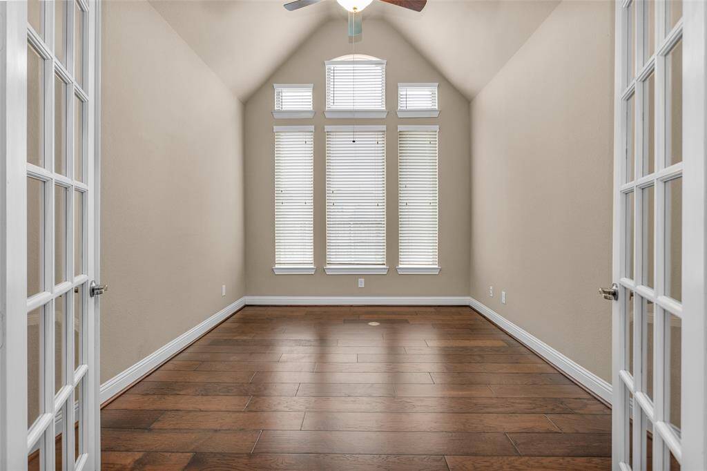 The study features a vaulted ceiling, abundant natural light from tall windows, French doors, and elegant hardwood flooring, creating a bright and inviting space.