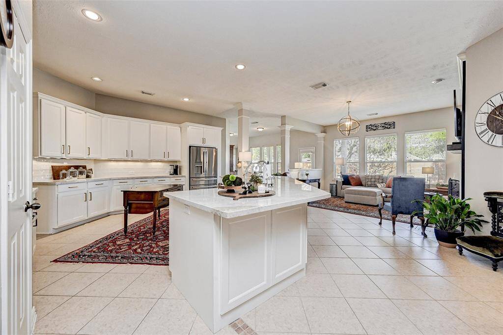 This photo showcases an open-concept kitchen and living area with modern white cabinetry and a central island. The space is light and bright due to large windows and recessed lighting.