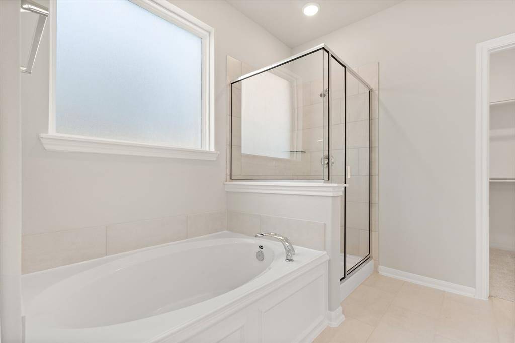 This additional view of your primary bathroom features tile flooring, fresh paint, walk-in shower, a separate garden tub, and a large walk-in closet.