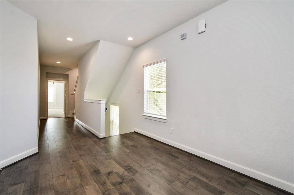 This photo showcases a modern, well-lit hallway with light gray walls and dark wood flooring. It features recessed lighting and a window, leading to a bright room at the end. The space is clean and contemporary, offering a blank canvas for personalization.
