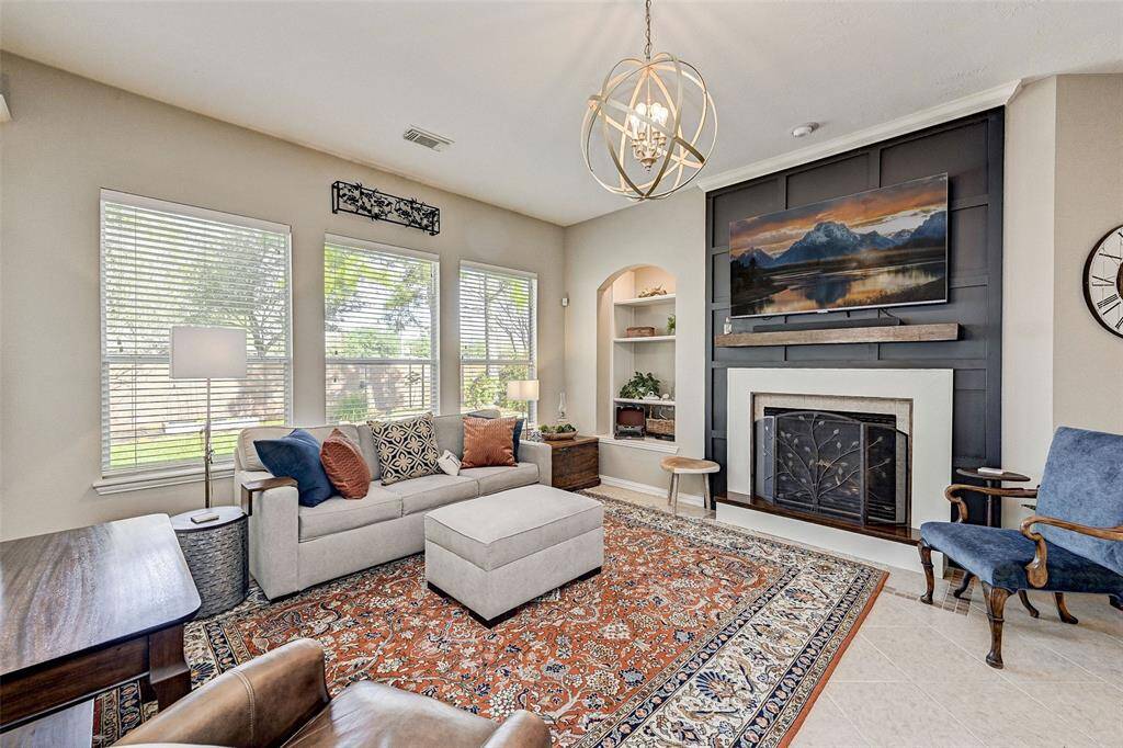 A cozy living room with ample natural light features a stylish chandelier and a decorative fireplace.  Large windows offer views of the outdoors, enhancing the airy feel.