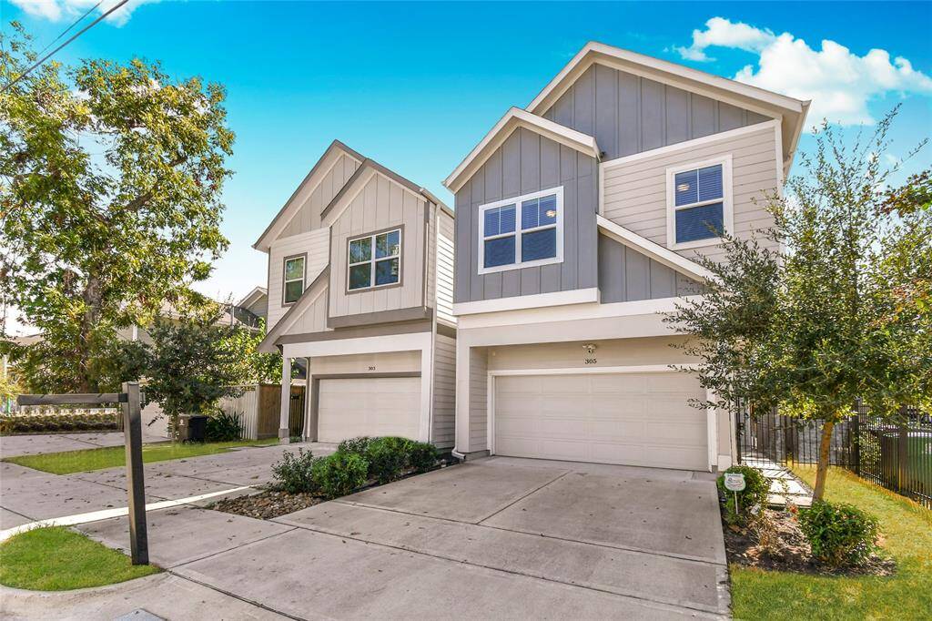 Modern three-story home with a clean exterior, featuring gray siding and white trim. It includes a double garage and a well-maintained driveway, surrounded by minimal landscaping and a tree.