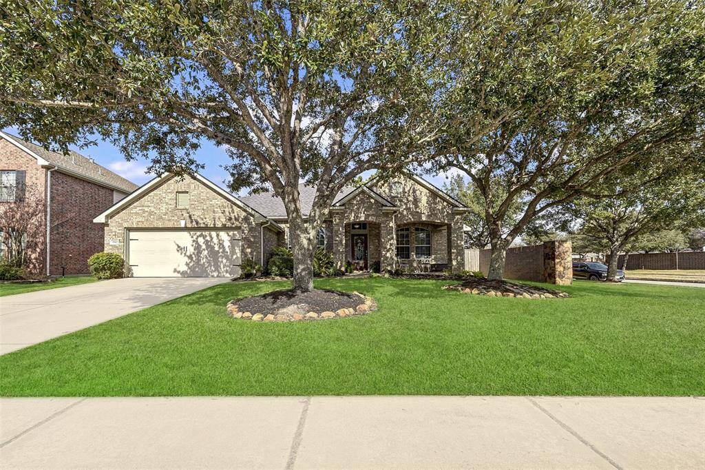 Charming single-story brick home with a spacious front yard, mature trees, and a two-car garage.