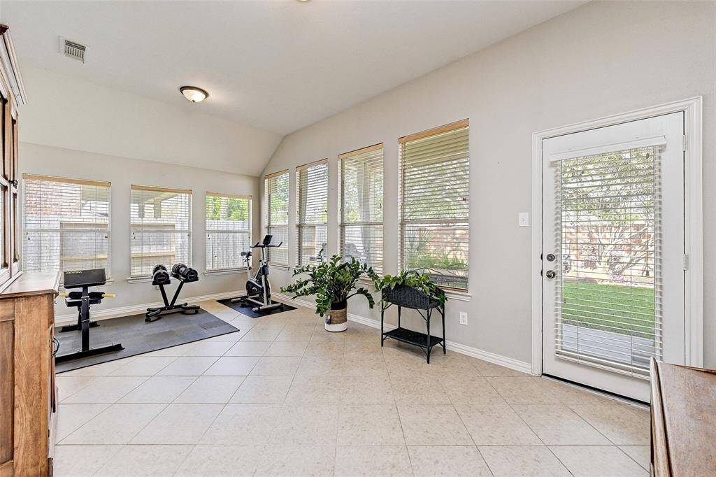 Bright, versatile room with large windows, tile flooring, and a door leading to the backyard. Currently set up as a home gym, offering plenty of natural light and space for personal use.