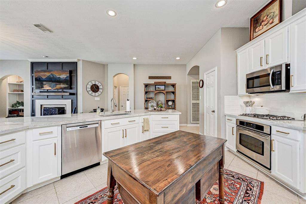 Another angle of spacious kitchen. Open layout with a view of the living area, featuring a fireplace and built-in shelves. Bright, with ample lighting.
