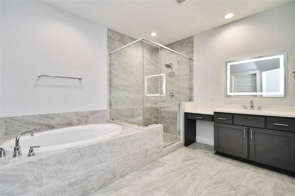 This bathroom features a modern design with a spacious glass-enclosed shower, a separate bathtub, and a sleek double vanity with dark cabinetry. The room is finished with neutral tile flooring and walls, creating a clean and elegant look.