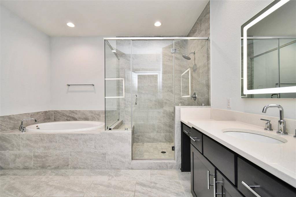 This is a modern bathroom featuring a glass-enclosed shower, a large soaking tub, and a double-sink vanity with sleek fixtures. The space is bright with neutral tile flooring and walls, providing a clean and contemporary look.