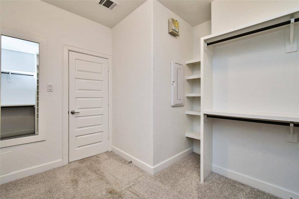 This photo shows a clean, carpeted walk-in closet with built-in shelves and hanging rods. It features a modern white door, a wall-mounted mirror, and ample storage space.