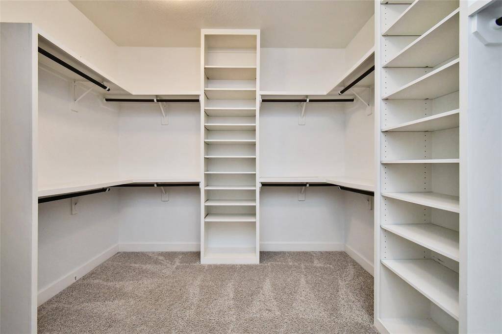 Spacious walk-in closet with ample shelving and hanging space, featuring a neutral color palette and carpeted flooring for a clean, organized look.