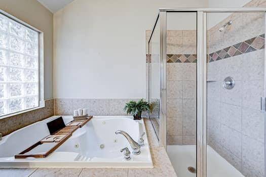 Primary bathroom also features a spacious tiled shower and a luxurious jetted tub with glass block window for natural light. Elegant fixtures and neutral tones create a relaxing atmosphere.