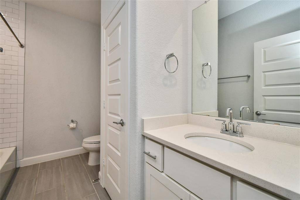 This modern bathroom features a sleek design with a white vanity, an undermount sink, and chrome fixtures. It includes a tiled shower-tub combination and neutral-toned floor tiles, creating a clean and inviting space.