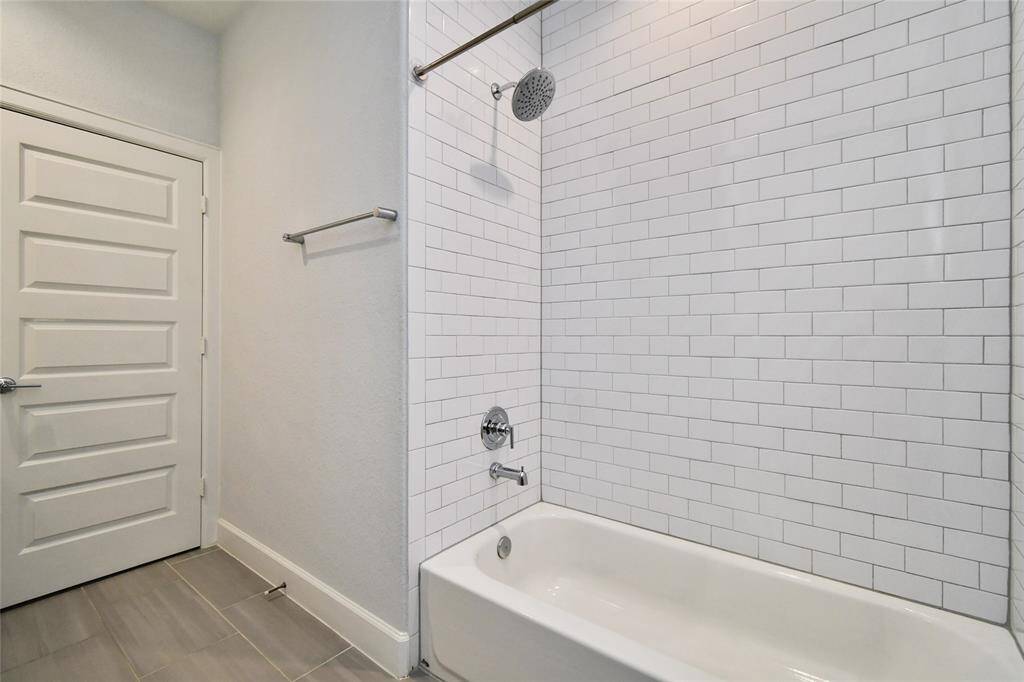 This bathroom features a modern design with white subway tile around the bathtub, a rainfall showerhead, and sleek gray floor tiles. The light-colored walls and door complement the clean, minimalist aesthetic.