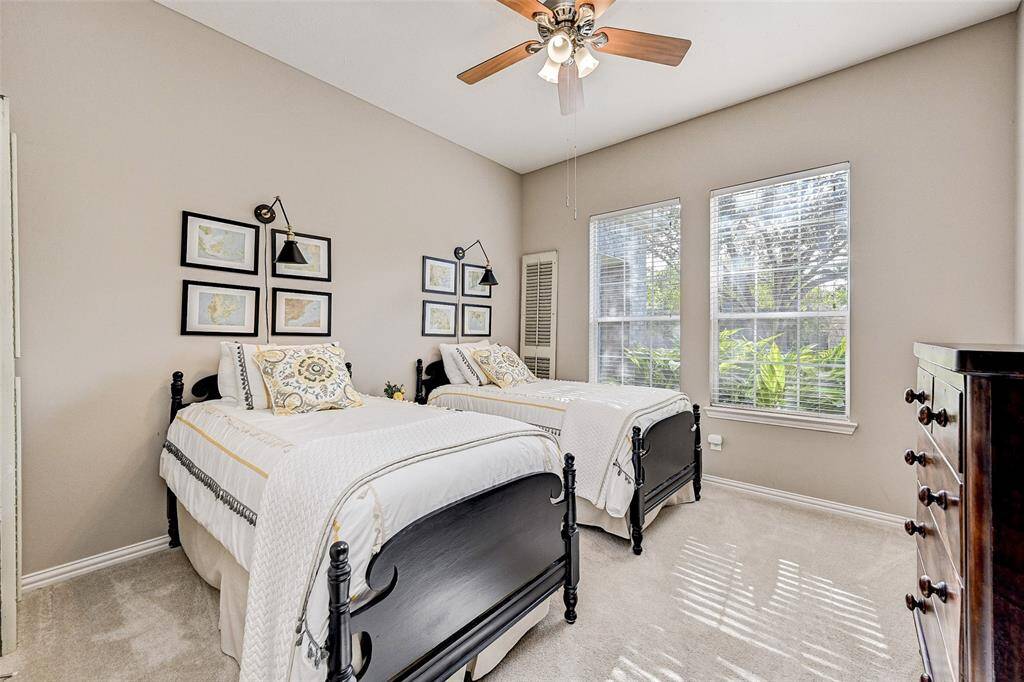 This cozy bedroom features neutral walls and abundant natural light from large windows. A ceiling fan adds comfort. Perfect for a guest or children's room.
