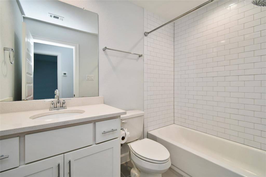 This is a modern bathroom featuring a sleek vanity with a large mirror, white cabinetry, and a bathtub with a classic white subway tile surround. The design is clean and contemporary, offering a fresh and inviting look.