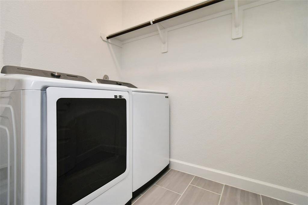 This photo shows a modern laundry room equipped with a sleek washer and dryer. The space features neutral walls, tiled flooring, and a convenient shelf for storage.