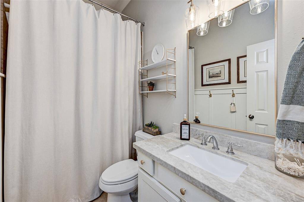 Secondary bathroom features a modern vanity with a marble countertop, a large mirror with stylish lighting, and a shower/tub combo.