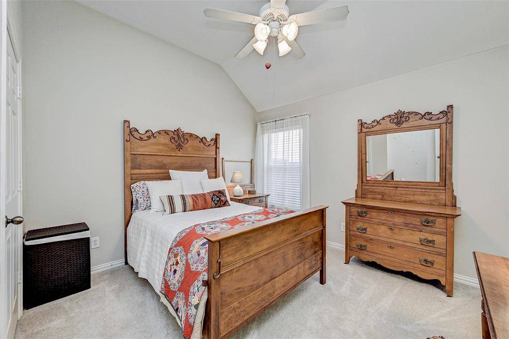 This bedroom features soft carpeting and a ceiling fan for comfort. Natural light fills the room through a window, giving it an inviting atmosphere.