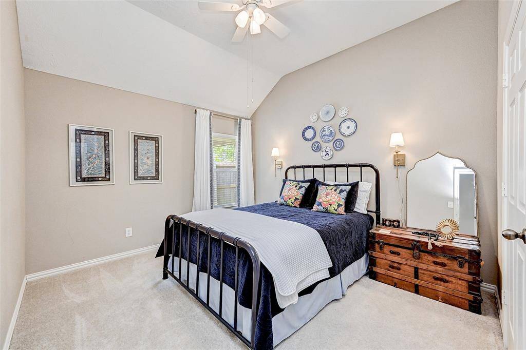 This cozy bedroom features a vaulted ceiling, neutral walls, and plush carpeting. A large window allows natural light.