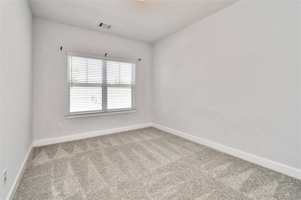 This is a bright, neutral-colored room featuring plush carpet and a large window with blinds, ideal for a cozy bedroom or office space.
