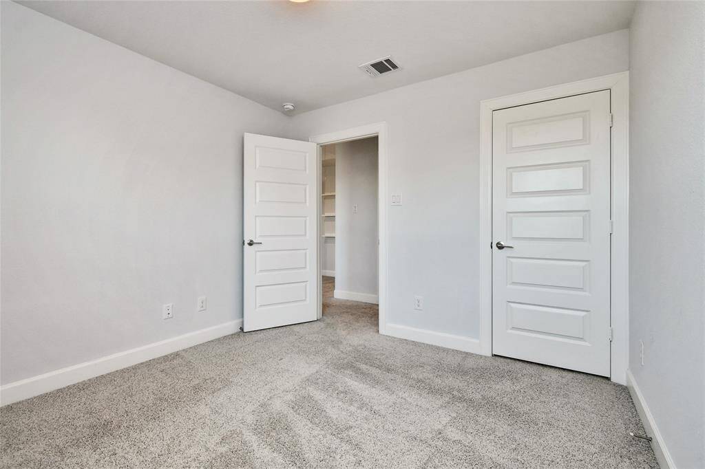 This photo shows a bright, neutral-toned bedroom with light gray carpet and white walls. It features two white paneled doors, one leading to a closet and the other to a hallway. The room has a modern, clean look suitable for customization.