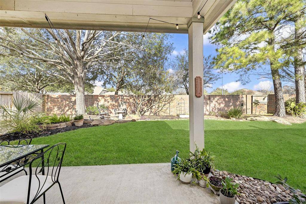 This photo showcases a serene backyard with a covered patio, lush green lawn, mature trees, and well-maintained landscaping. Ideal for outdoor relaxation and entertaining.