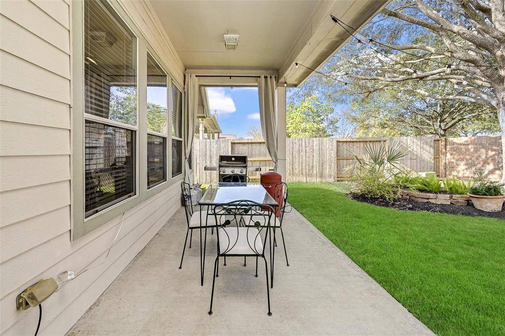 This cozy covered patio is adjacent to a well-maintained grassy backyard. There's a brick privacy fence creating an inviting outdoor space for relaxation and entertainment.