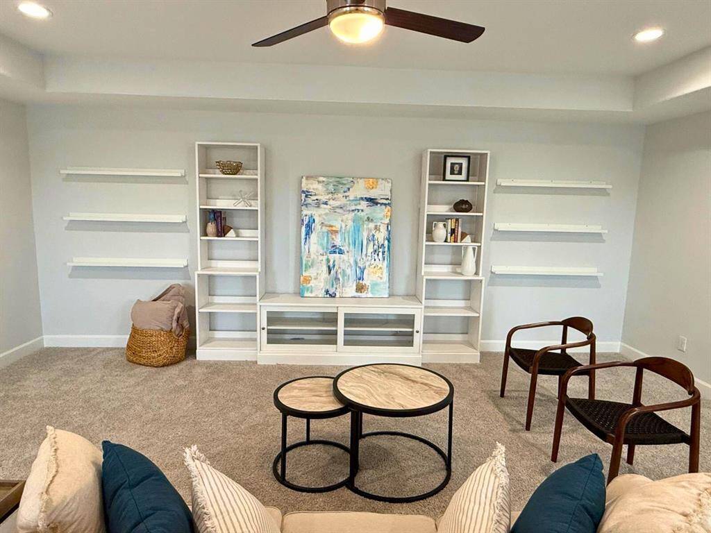 This cozy room features carpeted flooring, built-in shelves, and modern lighting. It includes stylish seating, a pair of nested coffee tables, and a decorative art piece, making it a perfect space for relaxation or reading.