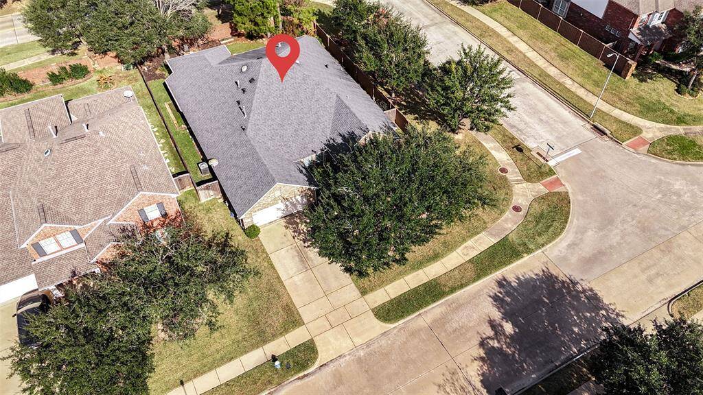 This aerial photo shows a corner-lot home with surrounding trees. The property features a double driveway which accommodates 4 cars and leads to a double garage and is located in a suburban neighborhood with sidewalks.