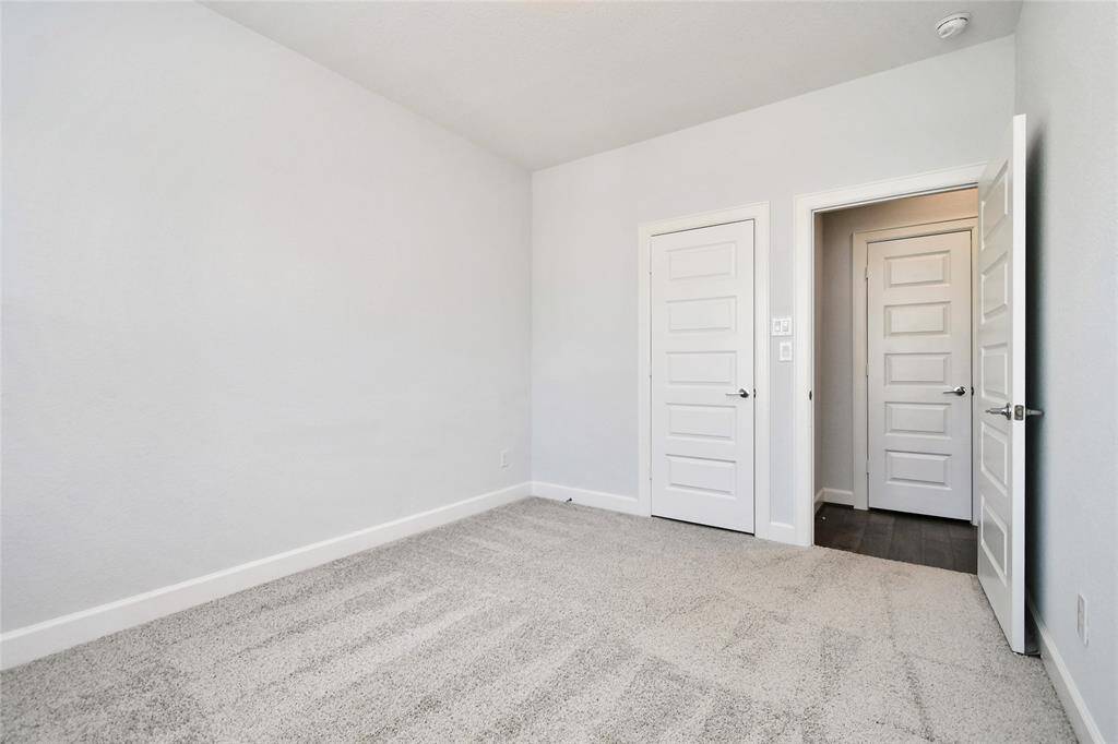 This photo shows a bright, empty room with light gray walls and carpeted flooring. There are two white paneled doors; one leads to another room or hallway, and the other is likely a closet. The space is clean and versatile, ideal for a bedroom or office.