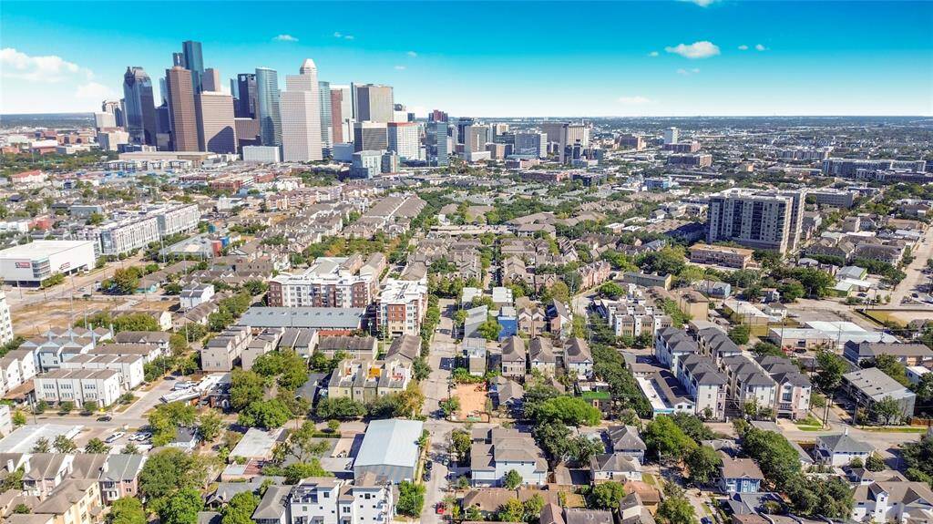 This aerial photo showcases a vibrant urban neighborhood with a mix of residential buildings and greenery, set against the backdrop of a large city skyline. Ideal for those seeking a balance of city living with accessible amenities and a sense of community.