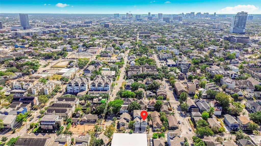Aerial view of a vibrant urban neighborhood featuring a mix of modern and traditional homes. The area is lush with greenery and centrally located, offering a clear view of a distant city skyline. Ideal for buyers seeking a lively community with easy city access.