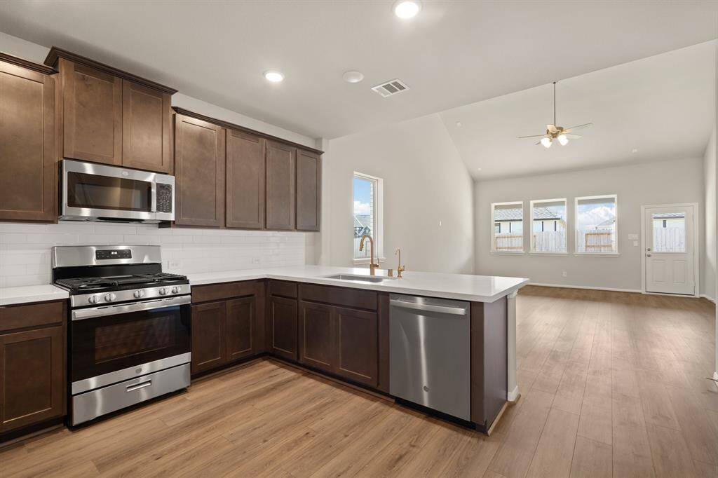 This light and bright kitchen features a large quartz island, dark stained cabinets, a large sink overlooking your family room, recessed lighting, and beautiful backsplash.