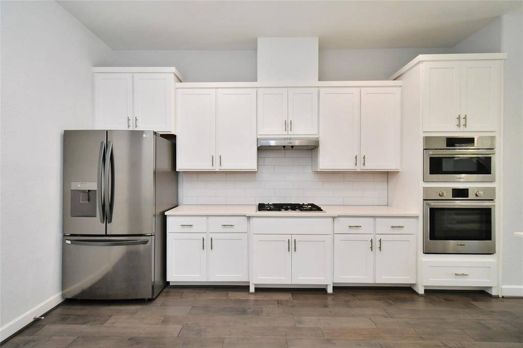 Modern kitchen with sleek stainless steel appliances, including a French door fridge and double oven. It features white cabinetry, a subway tile backsplash, and a gas cooktop, creating a clean, contemporary look.