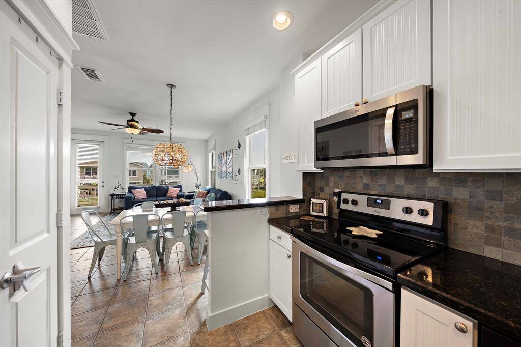 Cottage style cabinetry and stainless steel appliances in the kitchen with coastal lighting in living/dining.  Pantry behind the door on the left.