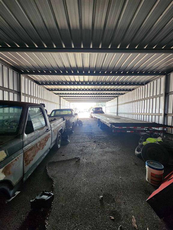 This is a spacious metal garage or storage unit with a high ceiling, housing several vehicles and a trailer. The structure appears sturdy and well-lit from natural light at the entrance. Ideal for vehicle storage or a workshop.