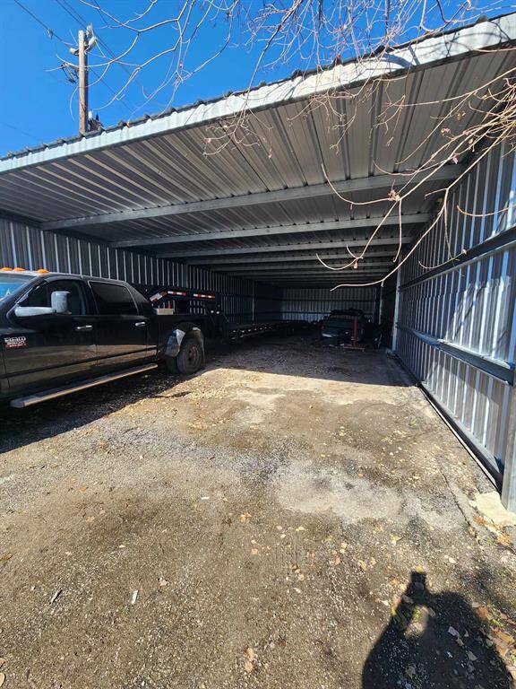 This photo shows a large, open metal carport with ample space for multiple vehicles, featuring a gravel floor and partial enclosure on three sides.