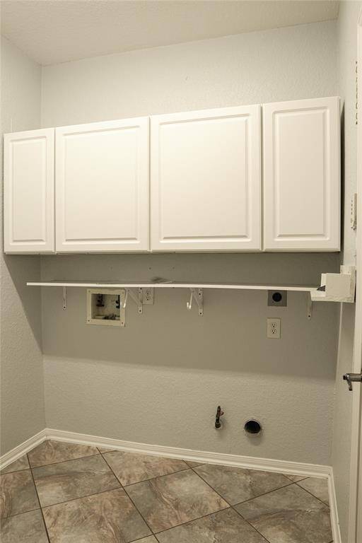 This photo shows a utility room with light-colored walls and tile flooring. It features three white wall cabinets for storage and hookups for a washer and dryer.